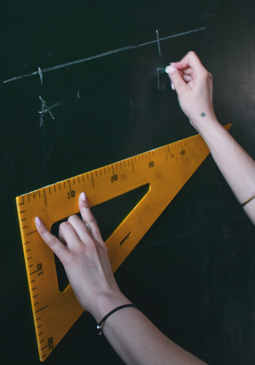 A math tutor measuring with a triangular ruler while writing on the chalkboard.